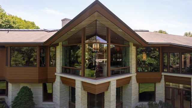 view of home's exterior featuring a shingled roof, a sunroom, and a chimney