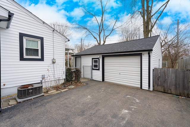 detached garage featuring aphalt driveway, fence, and central AC