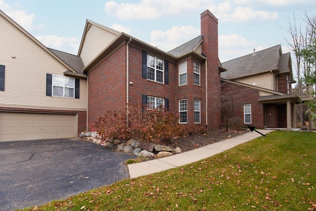 view of side of property featuring driveway, a yard, an attached garage, brick siding, and a chimney