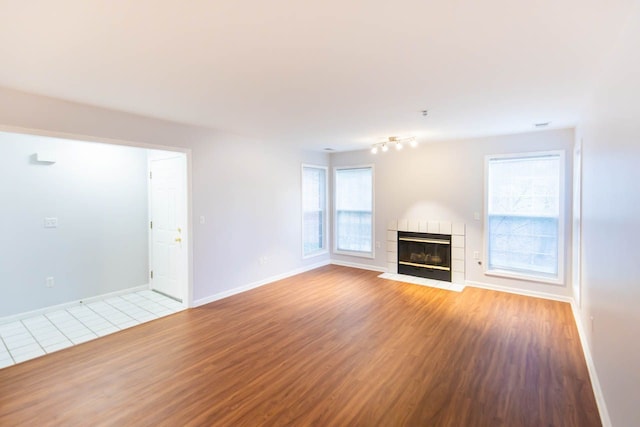 unfurnished living room featuring baseboards, wood finished floors, and a tiled fireplace