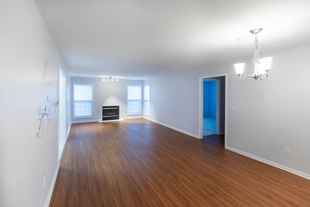 unfurnished living room featuring an inviting chandelier, a brick fireplace, baseboards, and dark wood-style flooring