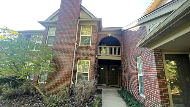 doorway to property featuring brick siding, a chimney, and a balcony