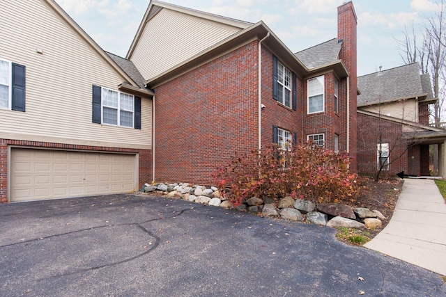 view of property exterior featuring brick siding, an attached garage, a chimney, and aphalt driveway