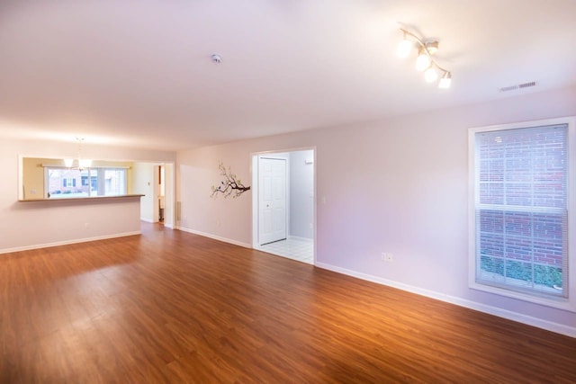 unfurnished living room featuring dark wood-style floors, visible vents, a notable chandelier, and baseboards