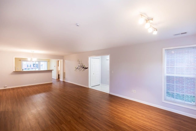 unfurnished living room with a notable chandelier, visible vents, baseboards, and dark wood-style flooring