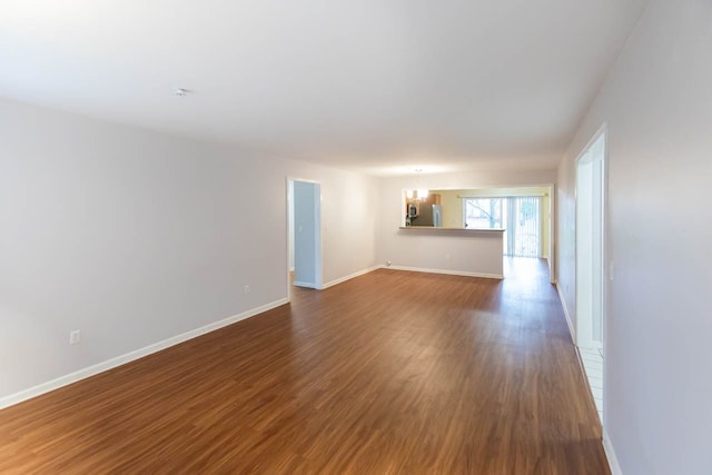 spare room featuring a chandelier, dark wood-type flooring, and baseboards