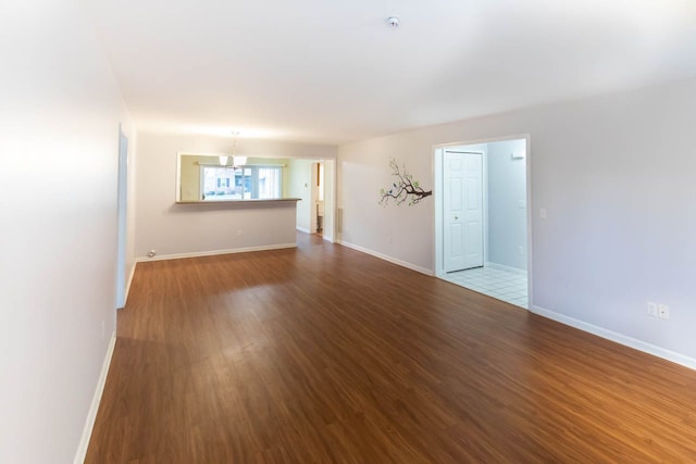 spare room with an inviting chandelier, baseboards, and dark wood-style flooring