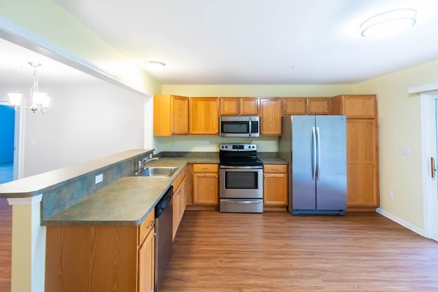 kitchen featuring light wood-style flooring, appliances with stainless steel finishes, a peninsula, a notable chandelier, and a sink