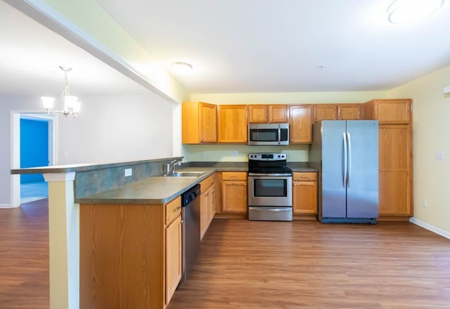 kitchen with a sink, light wood-style floors, appliances with stainless steel finishes, and pendant lighting