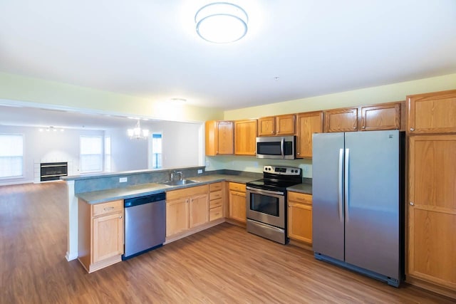 kitchen featuring open floor plan, light wood-style flooring, a peninsula, a fireplace, and stainless steel appliances