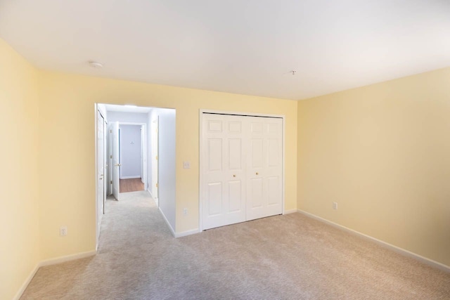 unfurnished bedroom with a closet, light colored carpet, and baseboards