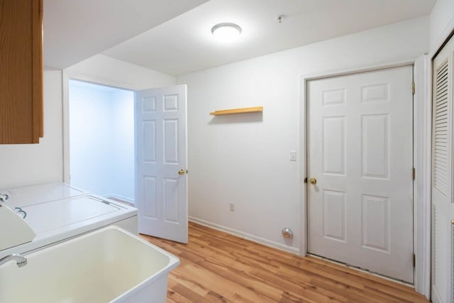 clothes washing area featuring light wood-type flooring, baseboards, separate washer and dryer, and cabinet space