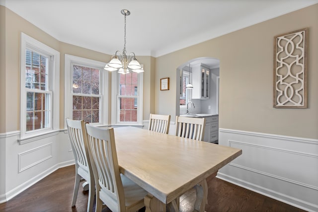 dining area with arched walkways, a wainscoted wall, dark wood-style flooring, crown molding, and a notable chandelier