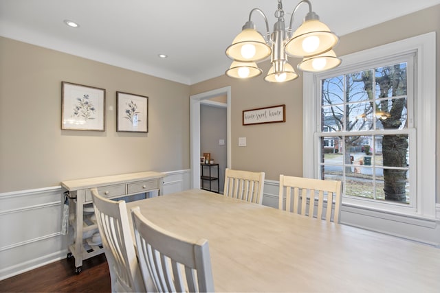 dining room featuring a healthy amount of sunlight, dark wood-type flooring, a notable chandelier, and wainscoting