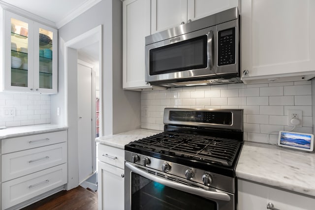 kitchen with white cabinets, ornamental molding, glass insert cabinets, light stone countertops, and stainless steel appliances