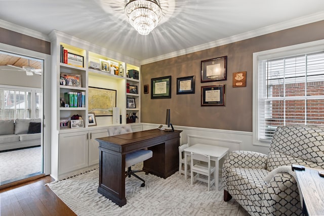 office area with built in shelves, a wainscoted wall, ornamental molding, hardwood / wood-style floors, and ceiling fan with notable chandelier