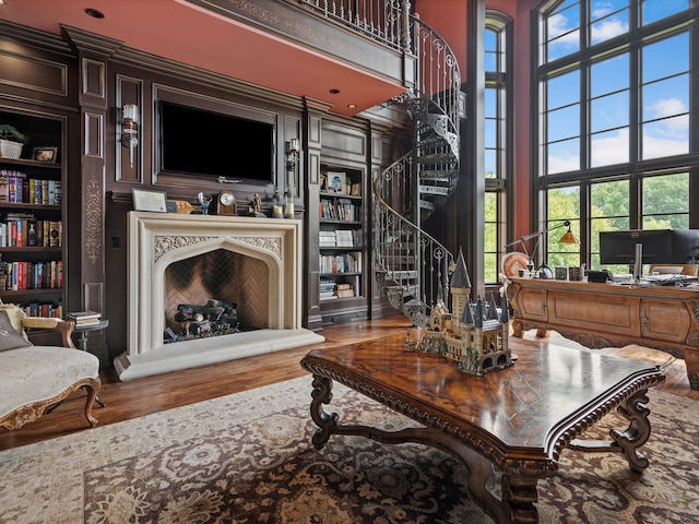 living room with built in shelves, a fireplace with raised hearth, stairway, a towering ceiling, and wood finished floors