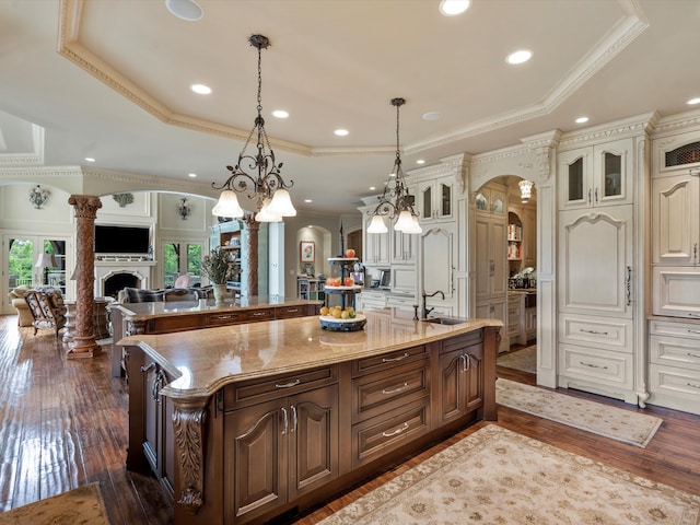 kitchen with arched walkways, a fireplace, open floor plan, a large island, and a raised ceiling