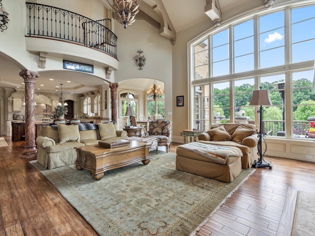 living room with ornate columns, a high ceiling, arched walkways, and hardwood / wood-style flooring