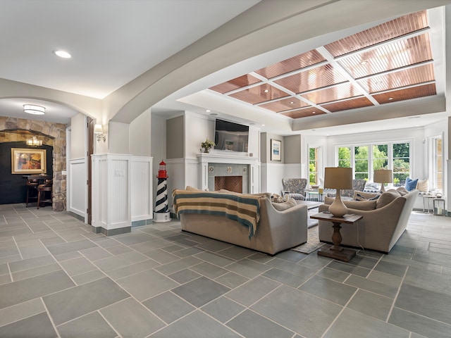 living area with a wainscoted wall, a fireplace, arched walkways, and coffered ceiling