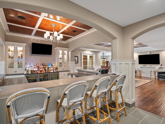 bar with a dry bar, coffered ceiling, wainscoting, wood finished floors, and an inviting chandelier