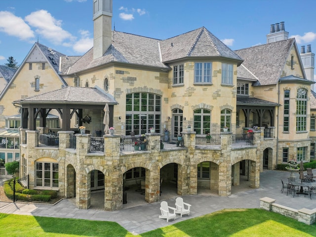 back of property with stone siding, a patio, and a balcony