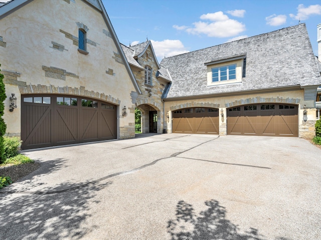 view of front facade with driveway, stone siding, and stucco siding