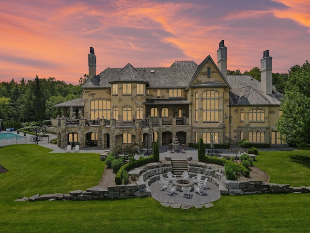 back of property with a patio, a balcony, a yard, stone siding, and a chimney