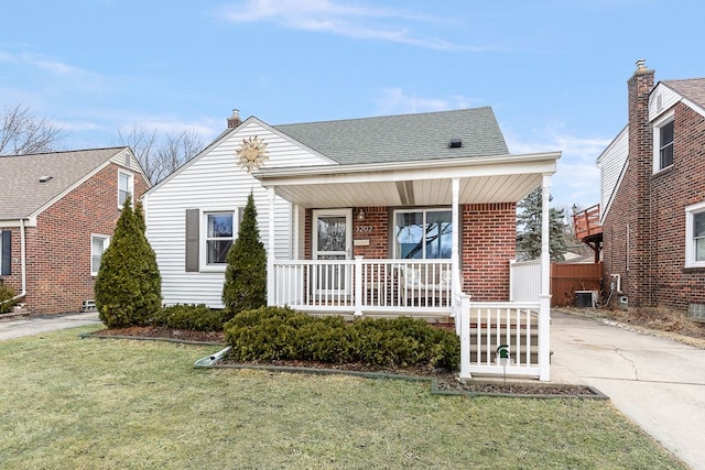 bungalow-style house with a front yard, covered porch, brick siding, and roof with shingles