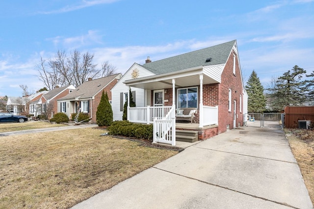 bungalow-style house featuring brick siding, covered porch, a gate, central AC, and a front yard