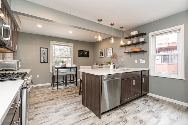 kitchen featuring dark brown cabinetry, stainless steel appliances, a sink, baseboards, and light countertops