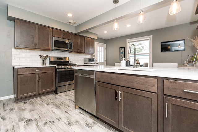 kitchen with a sink, light wood-style floors, light countertops, appliances with stainless steel finishes, and backsplash