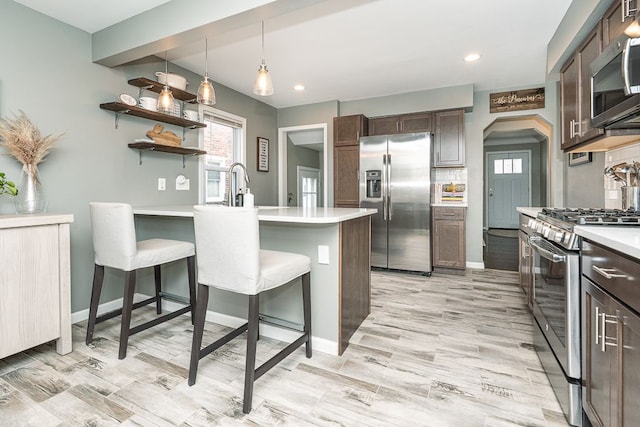 kitchen featuring dark brown cabinetry, tasteful backsplash, a breakfast bar area, a peninsula, and stainless steel appliances