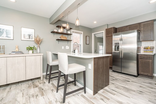 kitchen featuring stainless steel fridge, a peninsula, light countertops, dark brown cabinets, and a sink