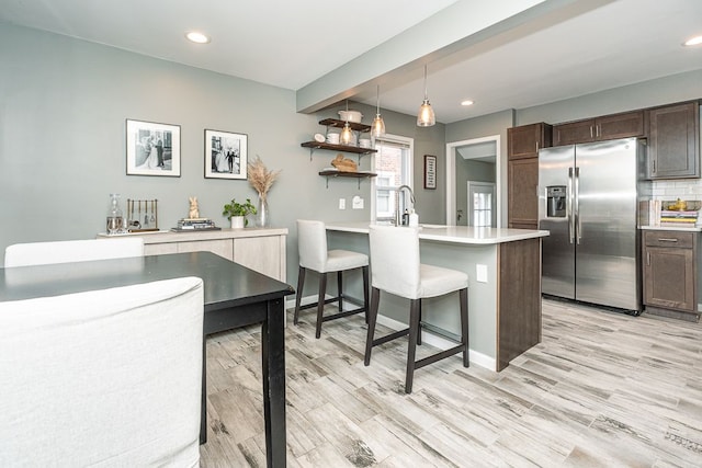 kitchen featuring a peninsula, light wood-style floors, dark brown cabinets, tasteful backsplash, and stainless steel fridge