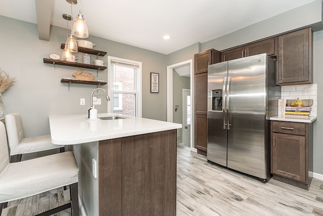 kitchen featuring a sink, dark brown cabinets, light countertops, stainless steel refrigerator with ice dispenser, and open shelves