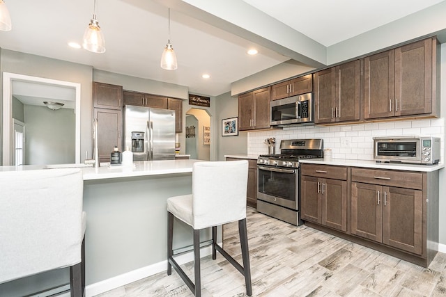 kitchen with arched walkways, a toaster, stainless steel appliances, light countertops, and decorative backsplash