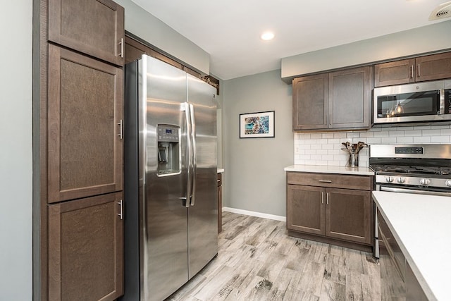 kitchen featuring stainless steel appliances, light countertops, backsplash, dark brown cabinetry, and light wood-type flooring