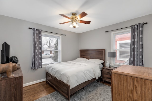 bedroom featuring ceiling fan, multiple windows, wood finished floors, and baseboards