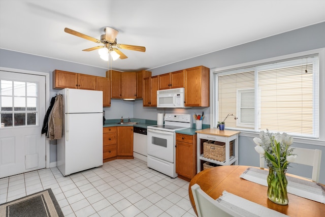 kitchen with a ceiling fan, brown cabinetry, light tile patterned flooring, a sink, and white appliances