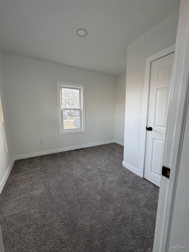 empty room featuring baseboards and dark colored carpet