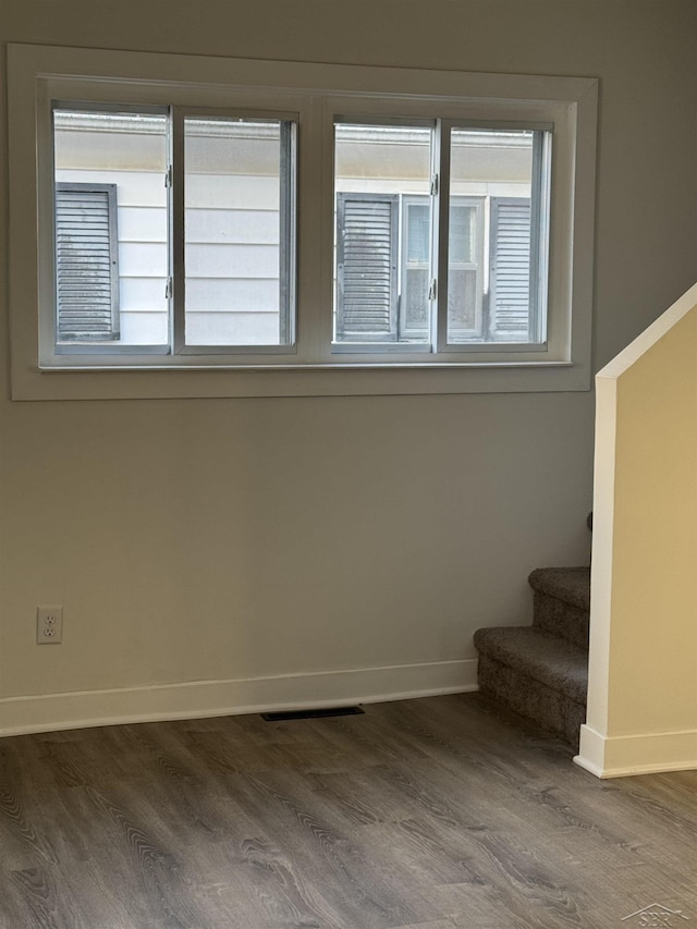 empty room featuring stairs, dark wood-type flooring, and plenty of natural light