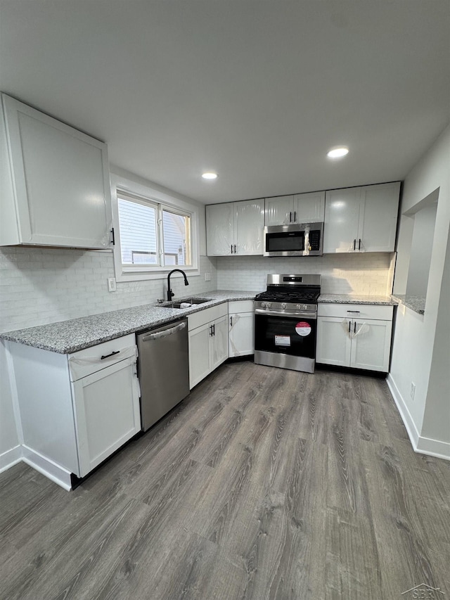 kitchen featuring light stone counters, dark wood-style flooring, stainless steel appliances, backsplash, and a sink