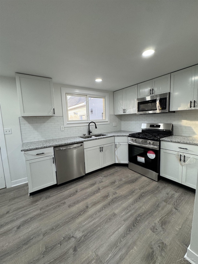 kitchen with stainless steel appliances, light wood finished floors, a sink, and white cabinets