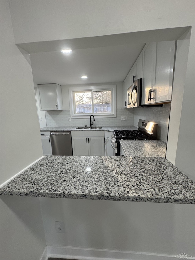 kitchen featuring tasteful backsplash, white cabinets, appliances with stainless steel finishes, light stone countertops, and a sink