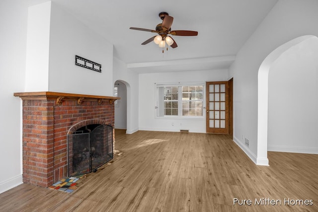 unfurnished living room with arched walkways, a brick fireplace, and wood finished floors