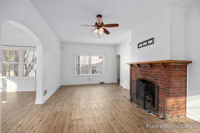 unfurnished living room with arched walkways, a ceiling fan, baseboards, a brick fireplace, and hardwood / wood-style floors