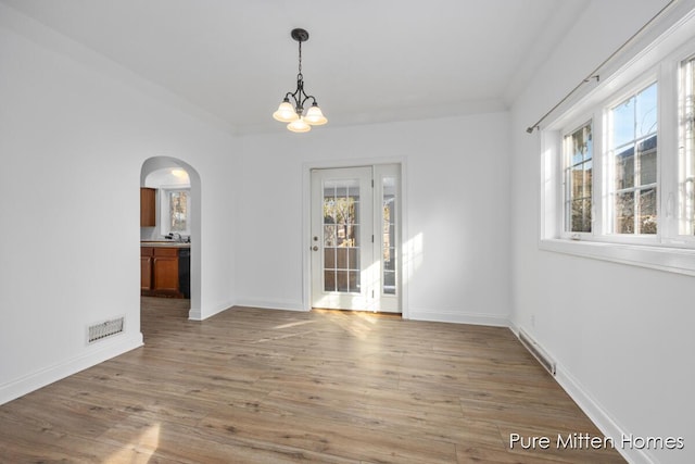 unfurnished dining area with arched walkways, a notable chandelier, visible vents, wood finished floors, and baseboards