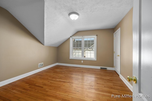 additional living space with baseboards, visible vents, a textured ceiling, and light wood finished floors