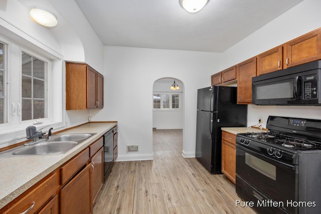 kitchen with arched walkways, light wood-style flooring, light countertops, black appliances, and a sink